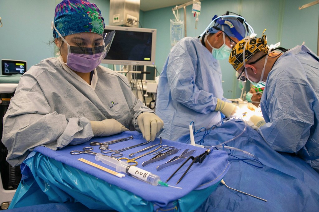 Surgical team operating while nurse prepares instruments on sterile field